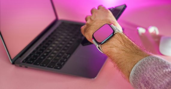A man holding a smart phone while using a laptop, illustrating businesses adopting hosted PBX