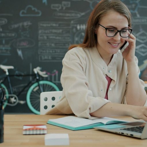 Woman talking on phone while working on laptop in office, illustrating hosted VoIP for SMEs