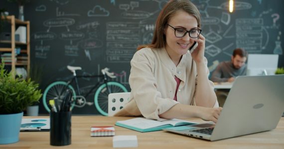 Woman talking on phone while working on laptop in office, illustrating hosted VoIP for SMEs