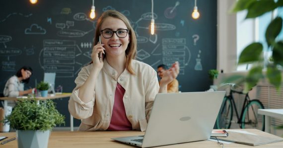 Smiling woman talking on phone in modern office, illustrating IP telephony for small business