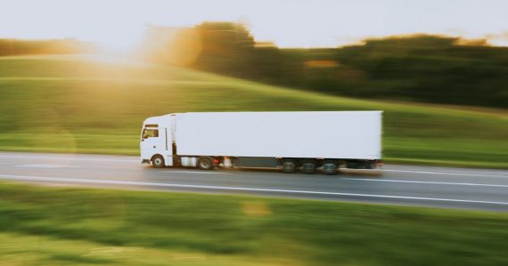 White semi truck driving down a rural road, illustrating cloud computing for transport and logistics