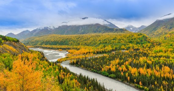 River beside forest under bright sky, illustrating local cloud support in Alaska