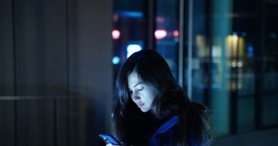 A woman in a blue jacket looking at her cell phone, illustrating mobile cloud computing market growth