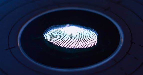 A glowing fingerprint on a dark scanner, illustrating identity, privacy and trust in the cloud