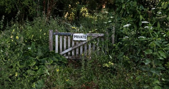 A weathered wooden gate with a PRIVATE sign in a dense garden, illustrating challenges in building private clouds