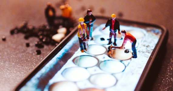 Tiny model construction workers working on a mobile phone screen, illustrating IT managers predicting cloud adoption