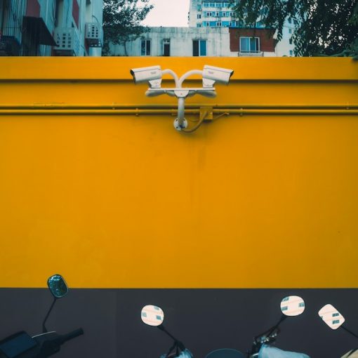 Vibrant yellow wall with security cameras above parked scooters, illustrating public cloud security advantages