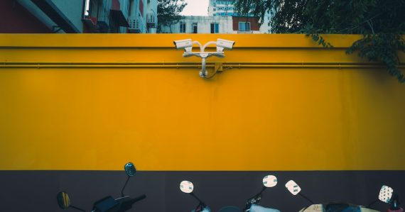 Vibrant yellow wall with security cameras above parked scooters, illustrating public cloud security advantages