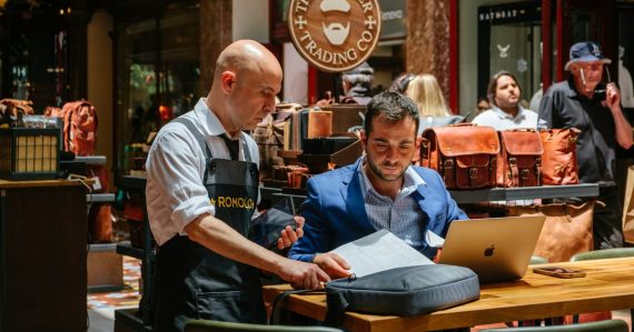 Two men looking at laptop and papers in store, illustrating deciding if SaaS fits a small business