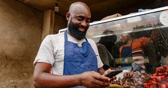 A shop owner in an apron looking at a cell phone, illustrating SaaS for small and mid-sized businesses