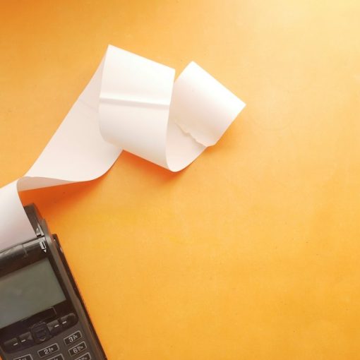 A black payment terminal with a long white paper receipt on orange background, illustrating sales tax and the cloud