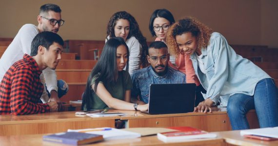 Group of students gathered around a laptop, illustrating schools turning to cloud computing