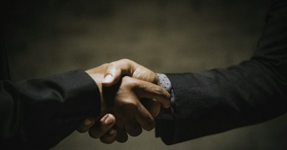 Two people shaking hands over a wooden table, illustrating building trust in cloud security
