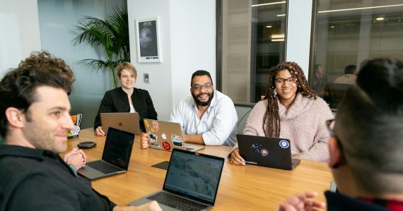 Four people on laptops listening to a speaker in a board meeting, illustrating VoIP and small business collaboration