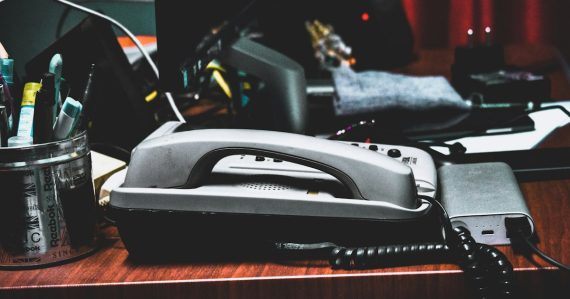 A desk with a phone, pencils, pens, and other office supplies, illustrating a small business guide to VoIP