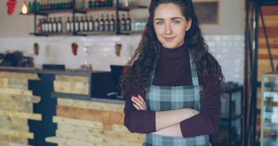 A smiling woman stands in her coffee shop, illustrating cloud computing and small business success