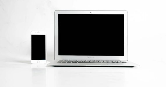 A white laptop computer sitting next to a cell phone, illustrating smartphones as laptop surrogates