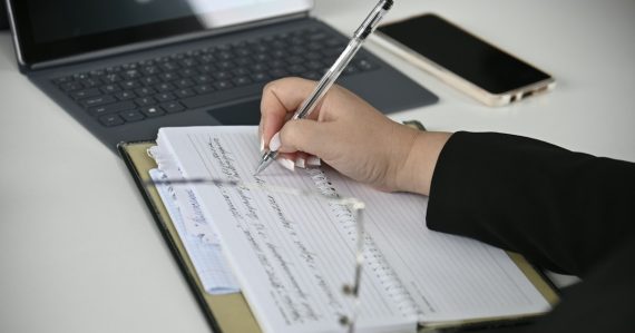 Person reviewing documents and writing notes, illustrating SOC 2 audit service standards