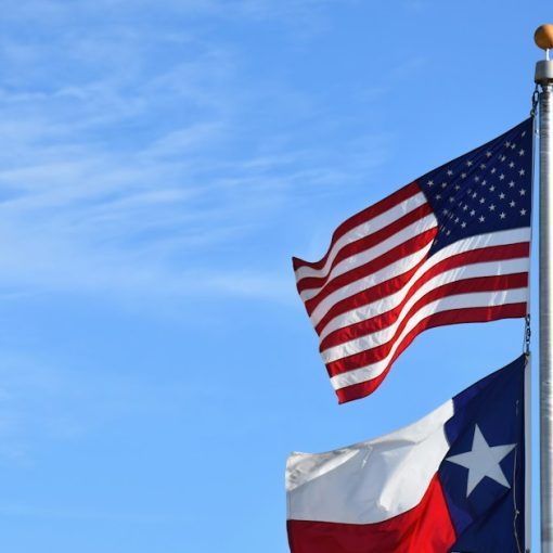 Two american and texas flags waving in the wind, illustrating VCE headquarters in Texas