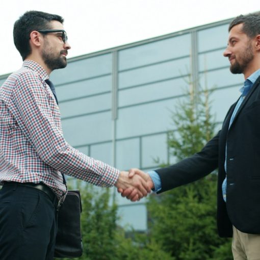 Two businessmen shaking hands outside modern building, illustrating growing trust in cloud computing