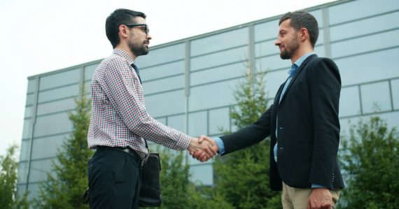 Two businessmen shaking hands outside modern building, illustrating growing trust in cloud computing