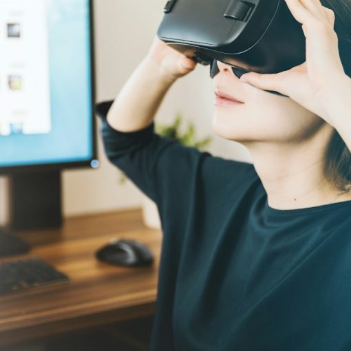 Woman using black VR headset beside computer, illustrating living with virtualization