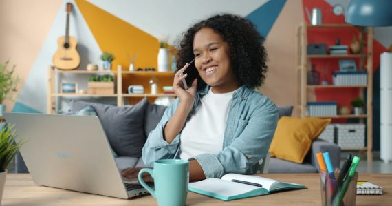 Woman talking on phone while working on laptop at desk, illustrating VoIP for small businesses
