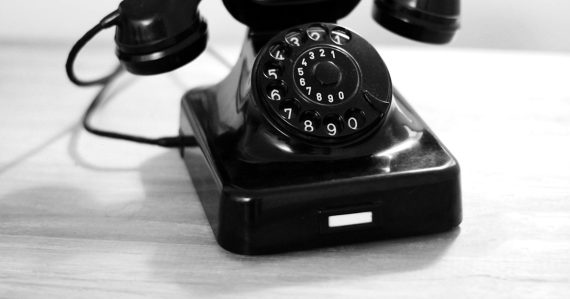 Black rotary phone on white table, illustrating VoIP replacing traditional telephony