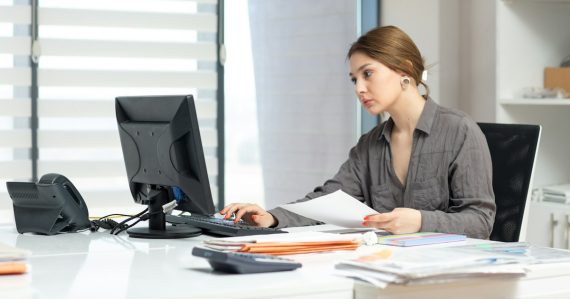 Young woman focused on computer and documents at office desk, illustrating choosing a VoIP service