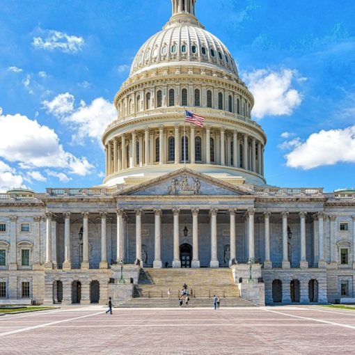 A large building with a dome and a flag on top with United States Capitol in the background, illustrating state taxes on VoIP