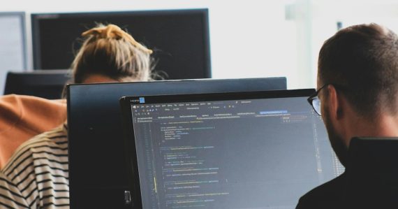 Two developers working on code at monitors in a bright office, illustrating service virtualization